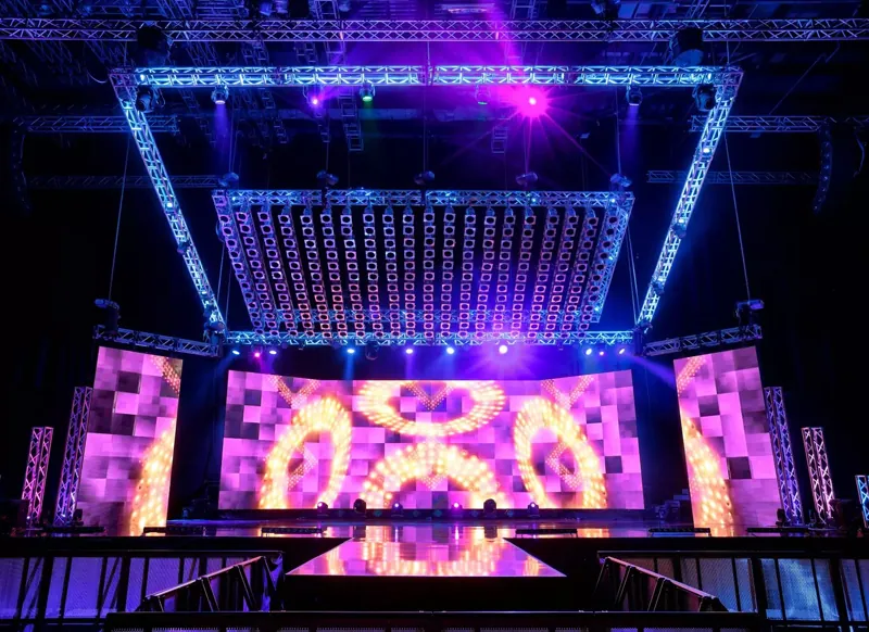 Arena stage under a full ground-support truss grid, LED wall running content behind the deck