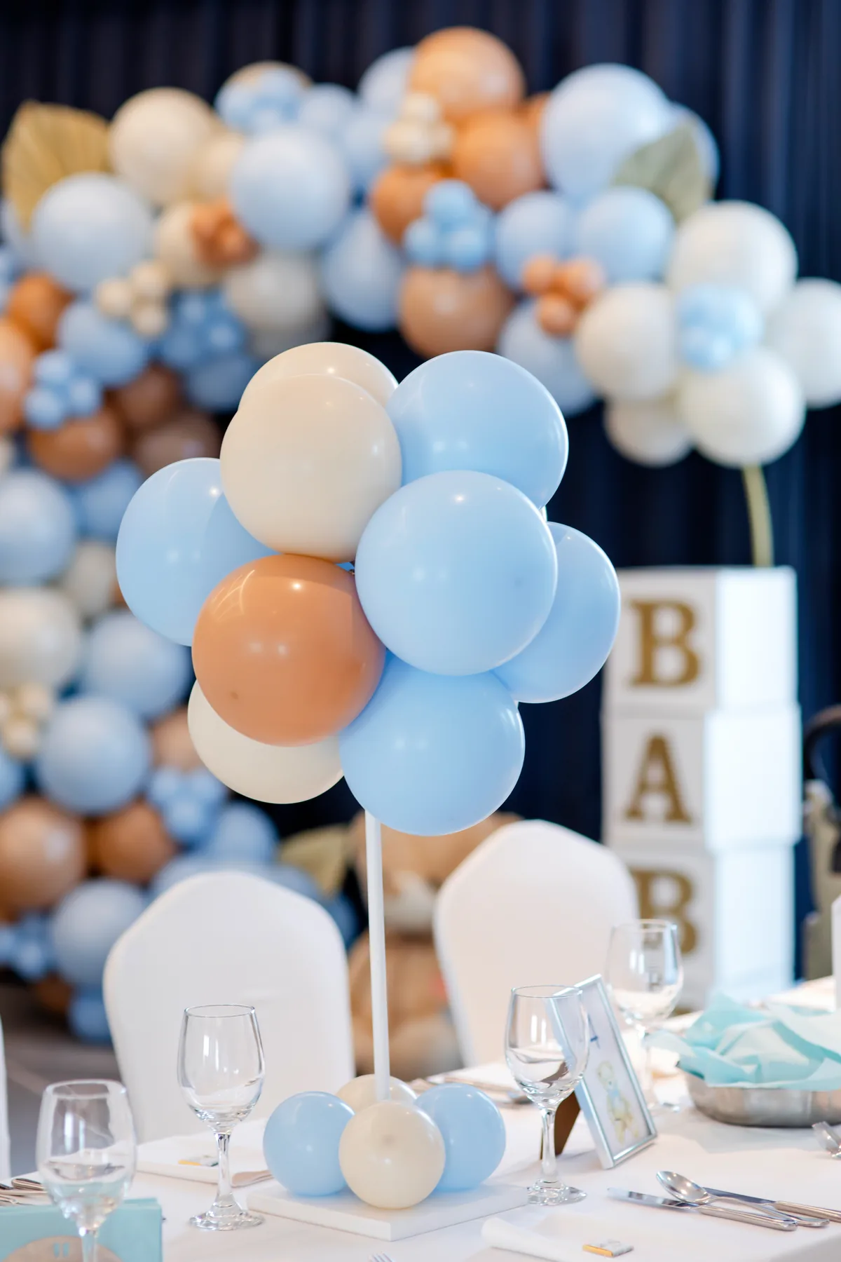 Baby shower table centrepiece of pastel blue, cream and peach balloons in front of a balloon arch and BABY letter blocks