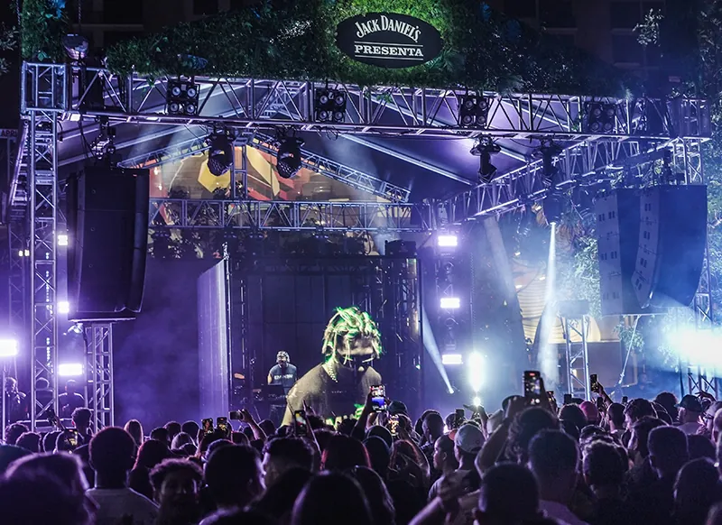 Branded outdoor festival stage lit in violet, truss towers and line array flown either side