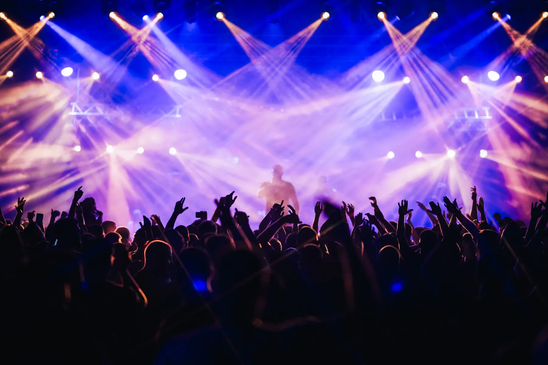 Crowd with hands raised under violet beams at a night event