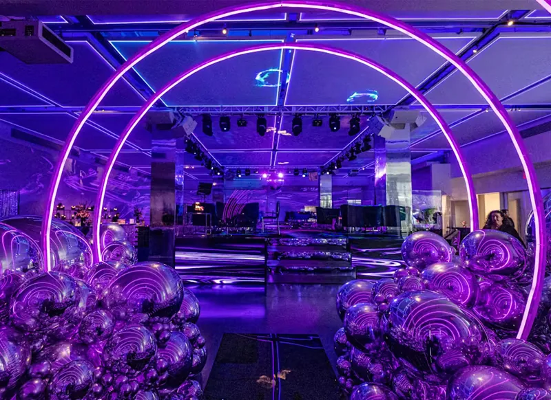 Balloon and decor installation in violet and chrome around a lit circular arch, venue floor set behind it