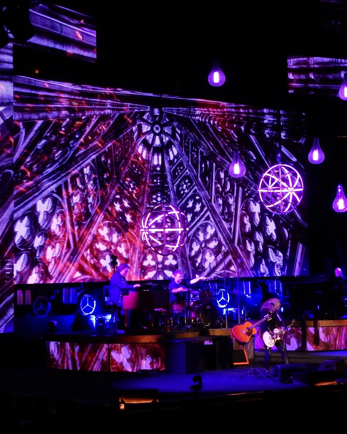 Concert stage backed by a full-height LED wall running cathedral imagery, with lit spheres and pendant globes hung in front of it