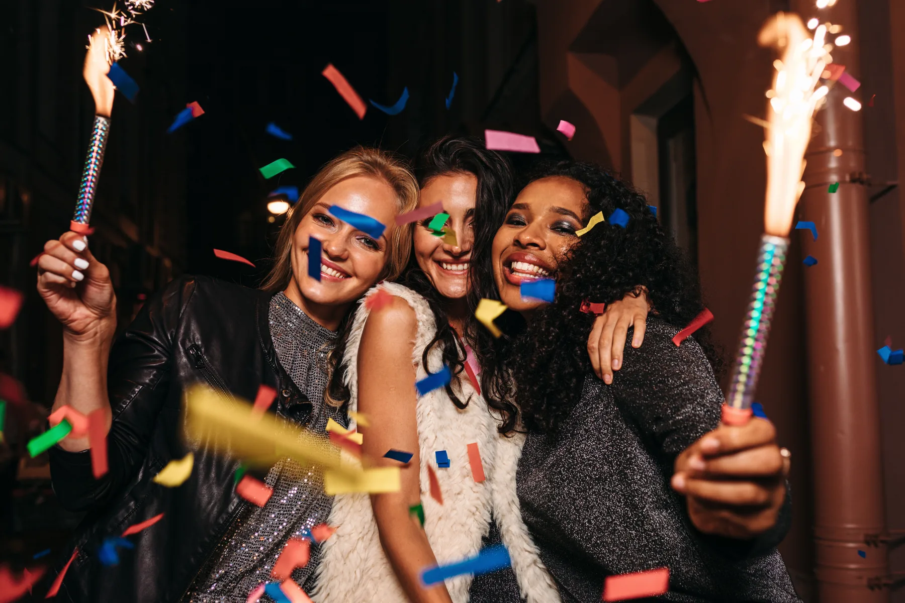 Three guests celebrating at night with sparkler candles and confetti falling around them