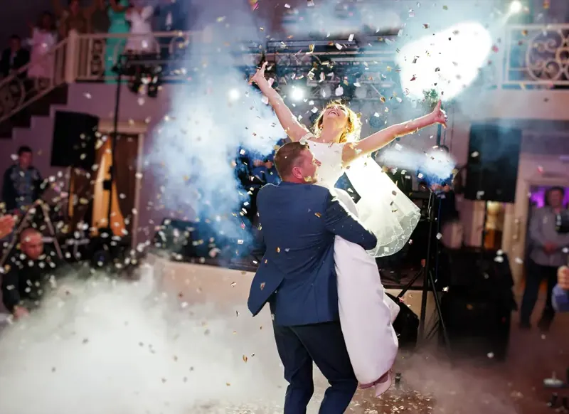 Bride and groom lifted mid-celebration on the dance floor as confetti and haze burst around them